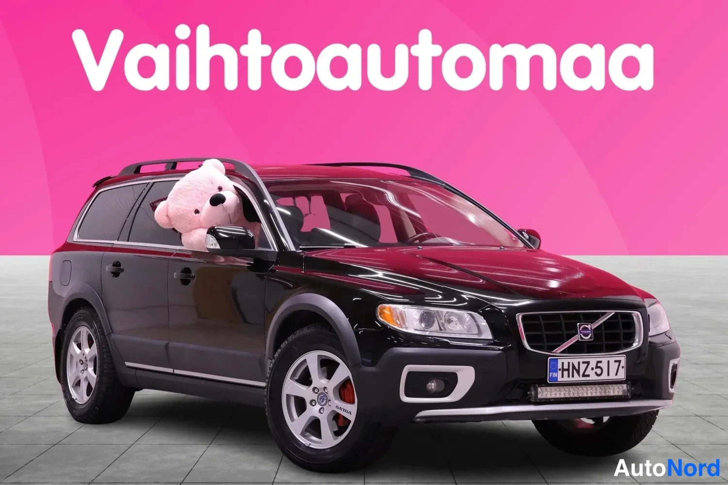 Etuviisto, nokka vasemmalle: Musta Volvo XC70, etuosa ja vasen kylki, edessä valkoiset kevytmetallivanteet ja katonrakennelma, ruudussa teksti Vaihtoautoma