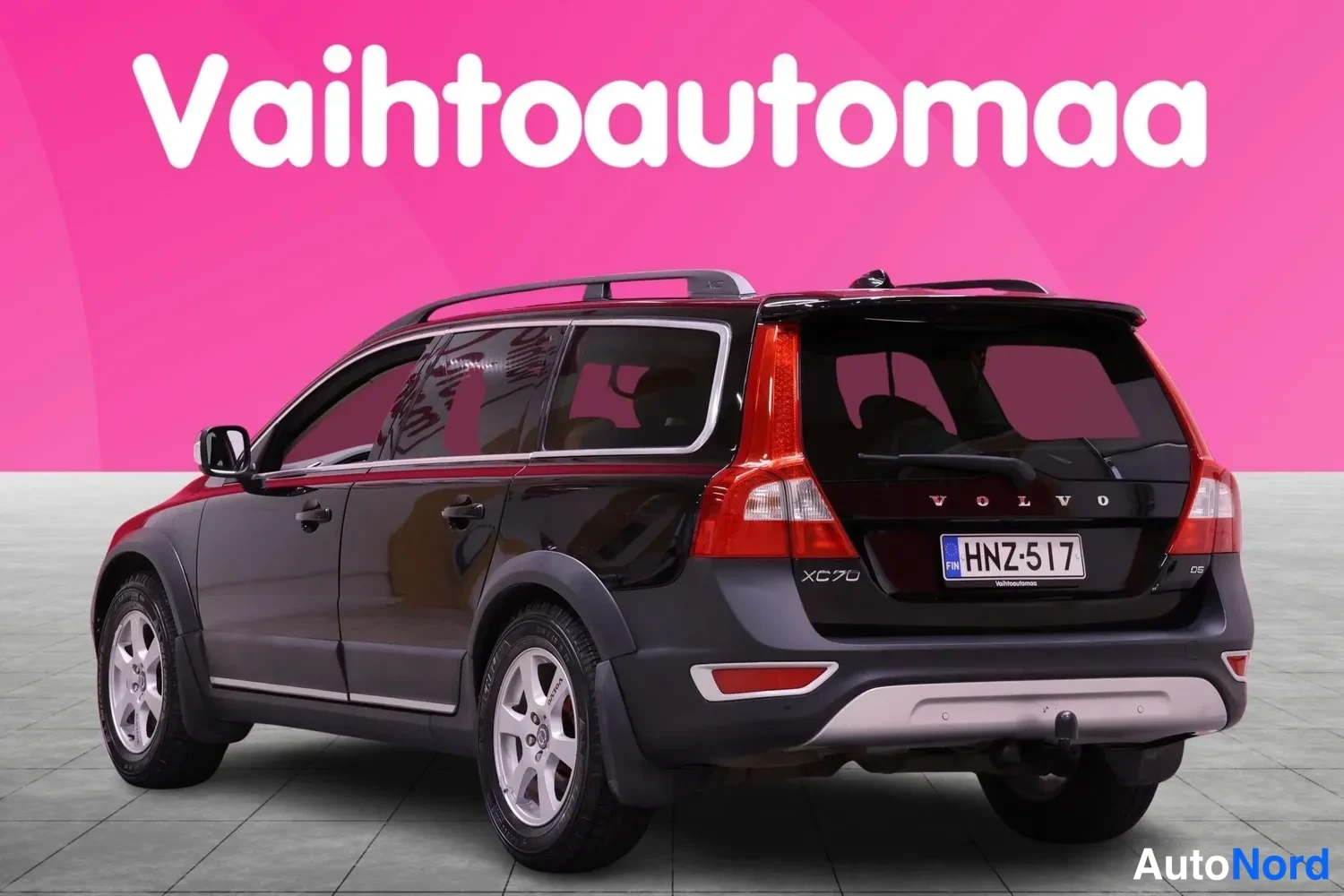 Takaviisto: Musta Volvo XC70 -farmariauto kuvaus takaa ja vasemmalta kulmasta. Auton takapää näkyy, mukana rekisterinumero ja katonrakot.