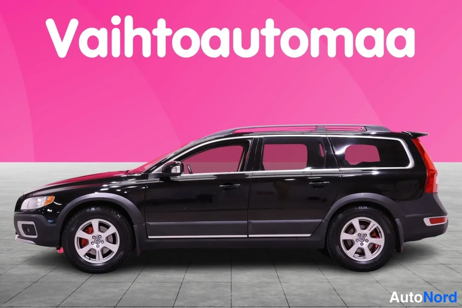 Sivulta: Musta Volvo XC70 -farmariauto sivulta kuvattuna. Kuvassa näkyy koko auton profiili, mukaan lukien etu- ja takapyörät sekä katonrakot.