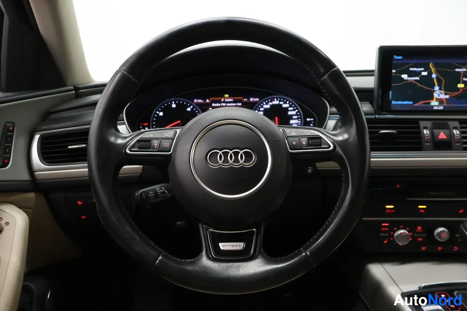 Yksityiskohta: Rattipaikan näkymä: Audi-ohjauspyörä ja mittaristo, MMI-navigaationäyttö kojelaudassa, tumma sisustus.
