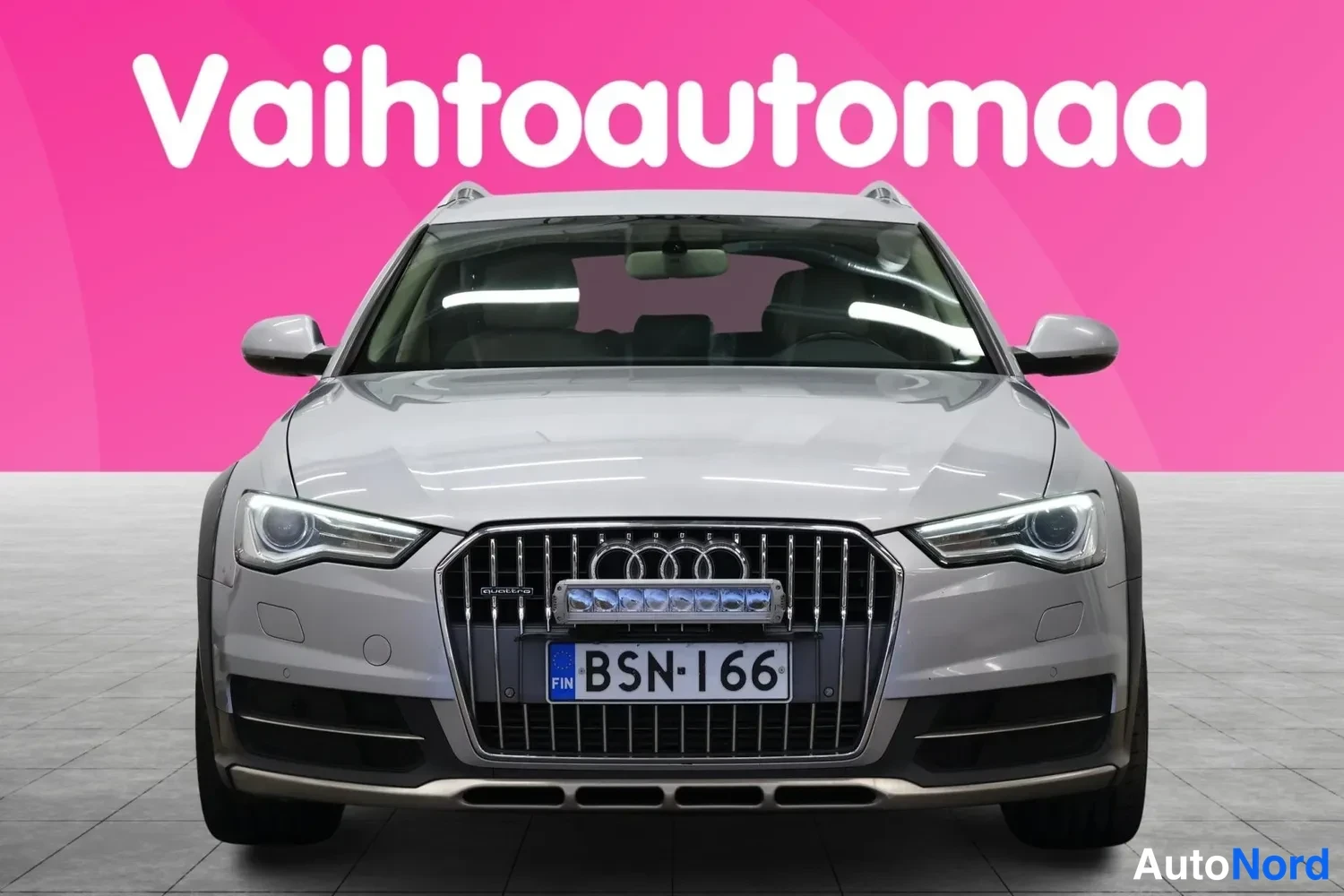 Edestä: Hopeanharmaa farmariauto suoraan edestä valokuvattuna, rekisterikilpi.