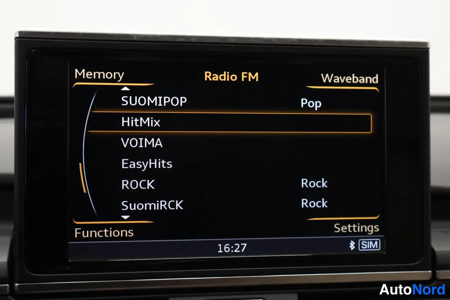 Yksityiskohta: Autoin päällä: MMI-näyttö, jossa Radio FM -valikko muistipaikoilla SUOMIPOP, HitMix, VOIMA, EasyHits, ROCK ja SuomiRCK. Kellonaika 16:27, näytössä Bluetooth- ja