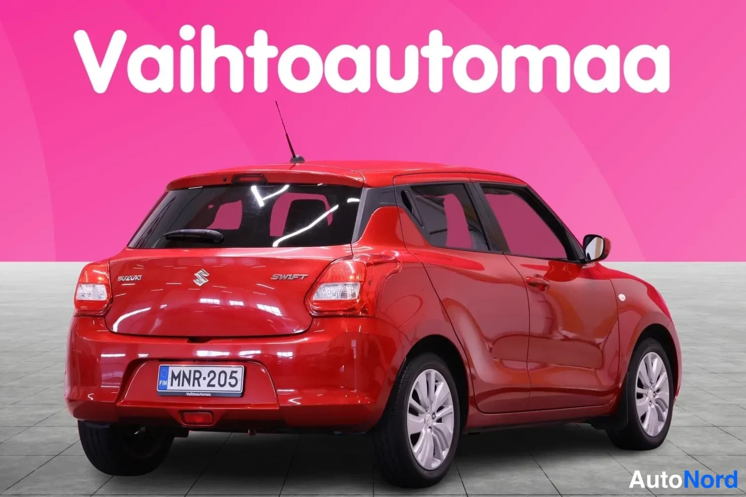 Takaviisto: Punaisen autotakan kokonaisnäkökulma oikealta puolelta. Takalukitusluukulla 'SWIFT'-teksti ja Suzuki-logo, sekä rekisterikilpi selvästi luettavissa.