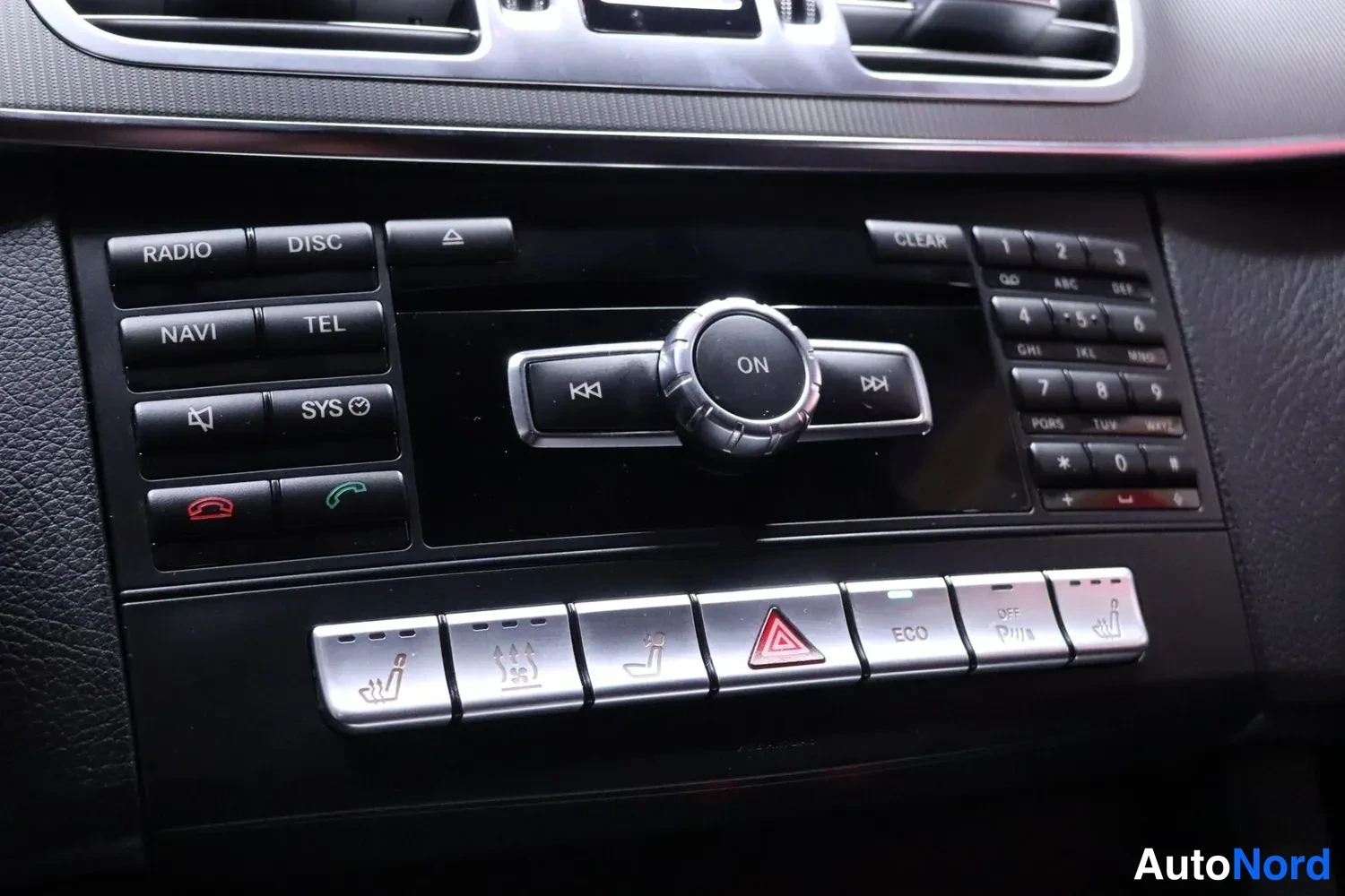 Muu: Mercedes-Benzin kojelaudan keskuskonsolin painikkeet: radio-, navigointi- ja puhelinpainikkeet, COMAND-ohjainkiekko sekä istuinlämmitys- ja ECO-painikkeet.
