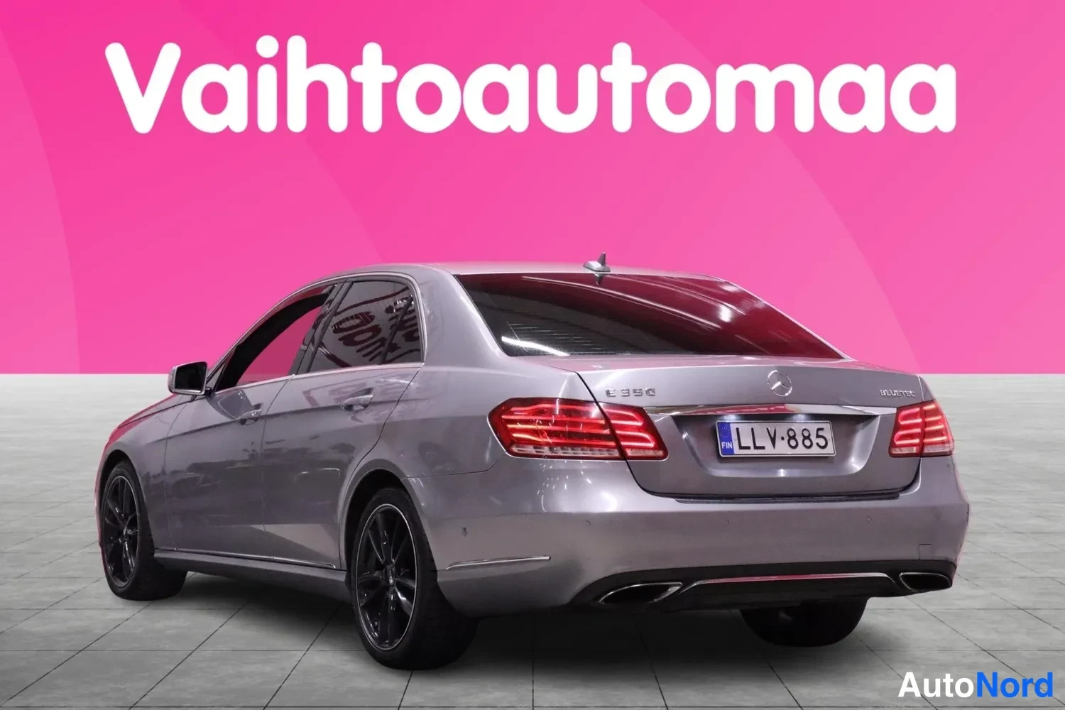 Takaviisto: Mercedes-Benz E-sarjan sedanin takaosa ja vasen kylki takaa sivulta kuvattuna; rekisterikilpi, harmaa hopeanvärinen kori.