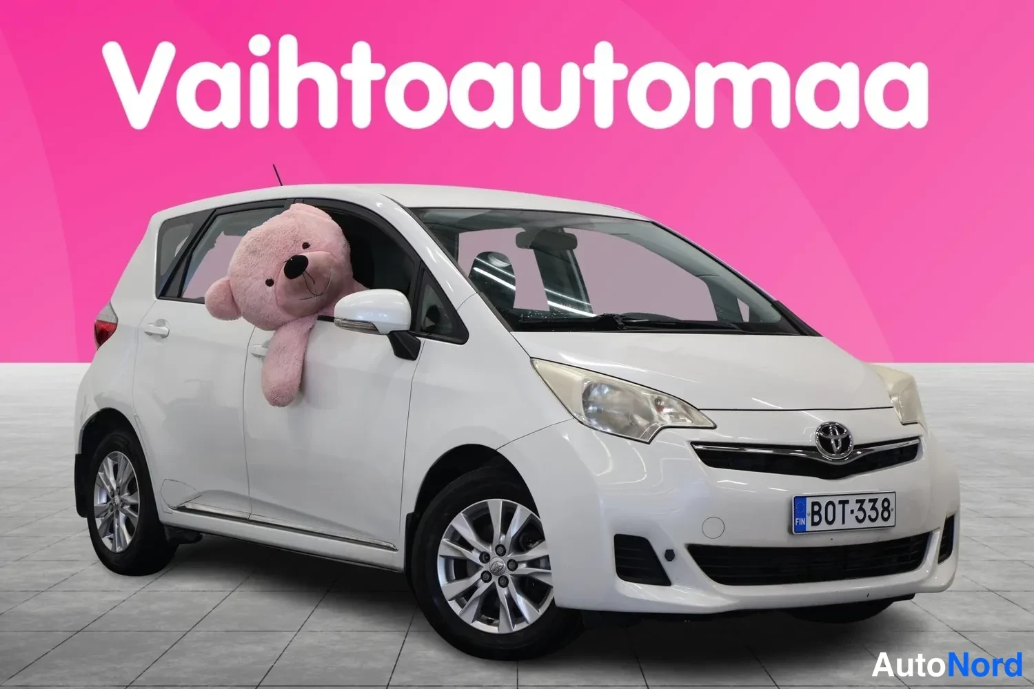 Etuviisto, nokka oikealle: Etukolmastonäkymä valkoisesta autosta, keula oikealla, nallekeino ikkunassa.
