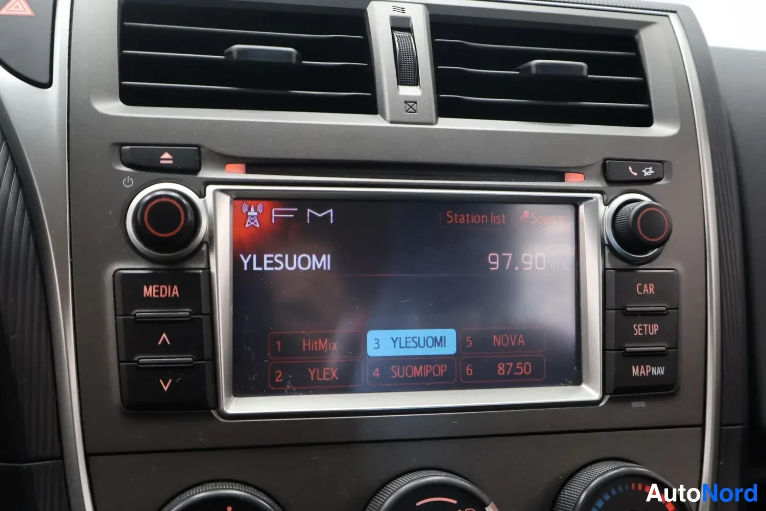 Muu: Auton kojelaudan keskikonsolin radio lähikuvassa: näytöllä FM-asemalista, valittuna kanava 3 YleSuomi taajuudella 97.90 MHz. Painikkeita Media, Car, Setup ja Ma