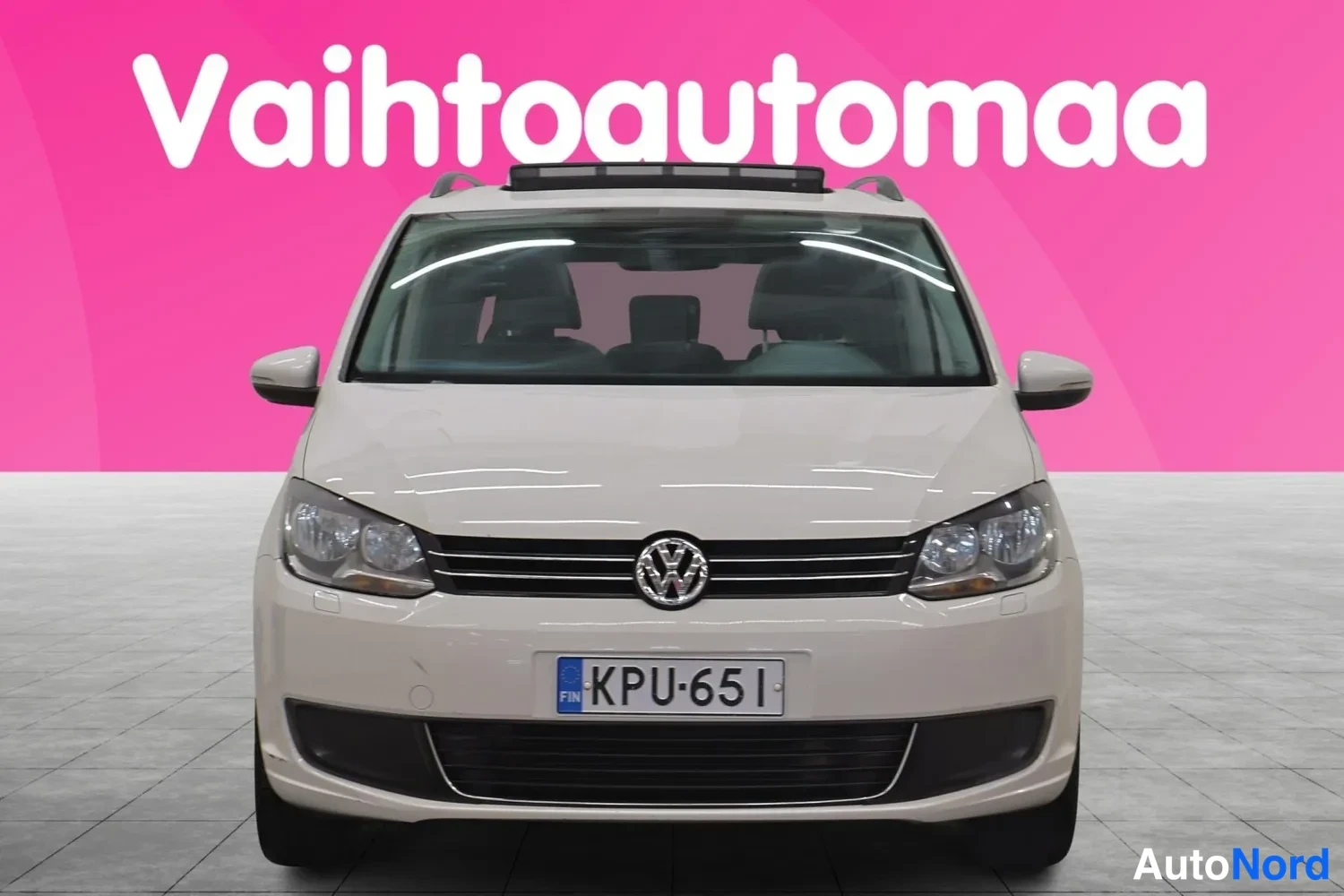 Edestä: Valkoinen Volkswagen Touran suoraan edestä kuvattuna, kohtisuora etunäkymä, rekisterikilpi.