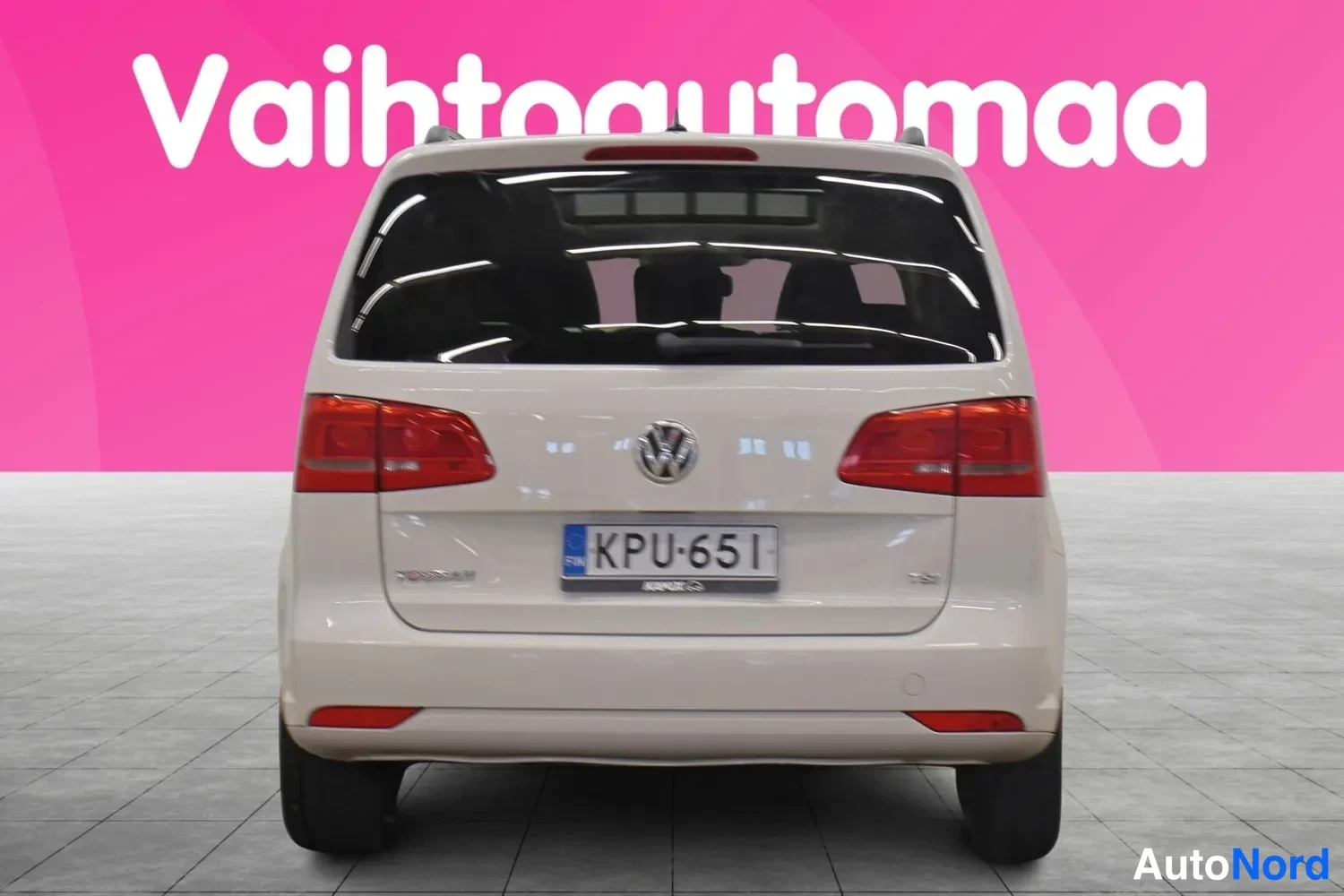 Takaa: Valkoisen tila-auton takaosa suoraan takaa, punaiset takavalot, VW-merkki ja rekisterikilpi.