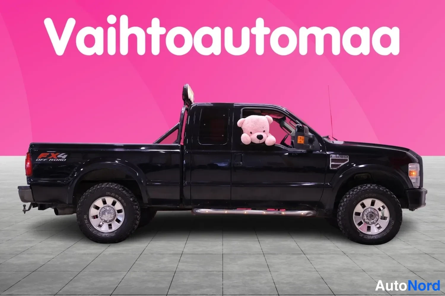 Etuviisto, nokka oikealle: Musta avolava-auto sivulta etukulmasta, keula oikealla, pinkki tausta.