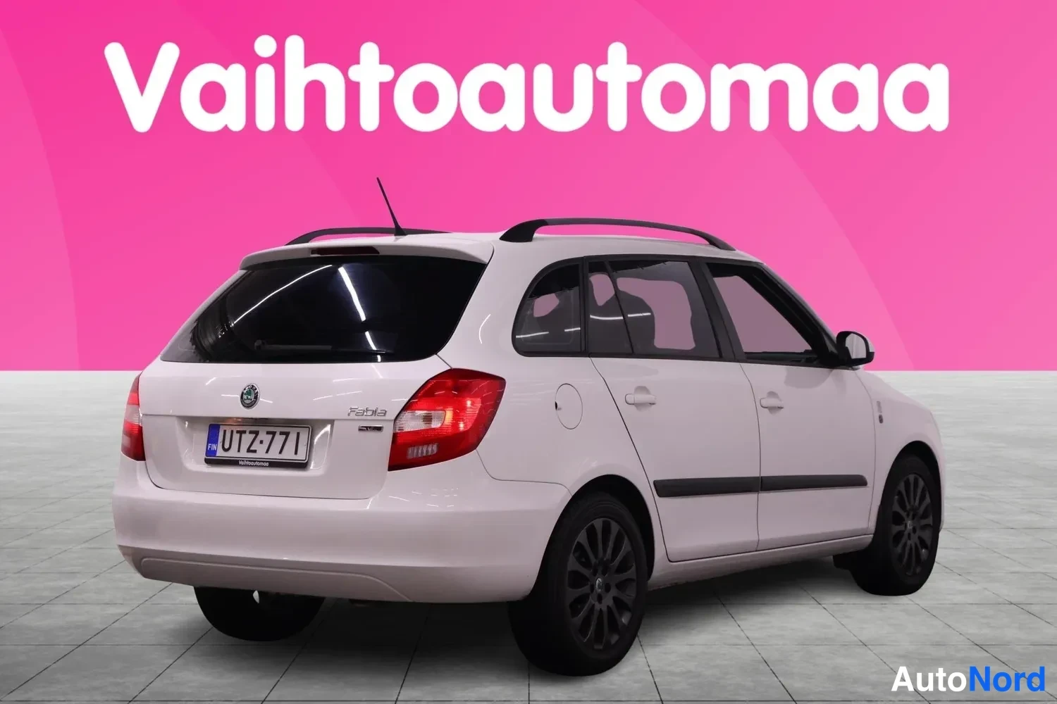 Takaviisto: Valkoinen Skoda Fabia -asema-auto takaa-%osakulmasta, rekisteritunnus, kattokaiteet ja tummat kevytmetallivanteet näkyvissä.