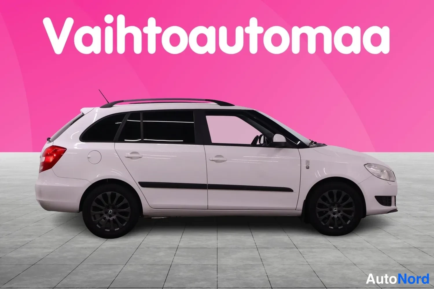 Takaviisto: Valkoinen Skoda Fabia -asema-auto sivulta, kattokiskot ja tummat kevytmetallivanteet näkyvissä.