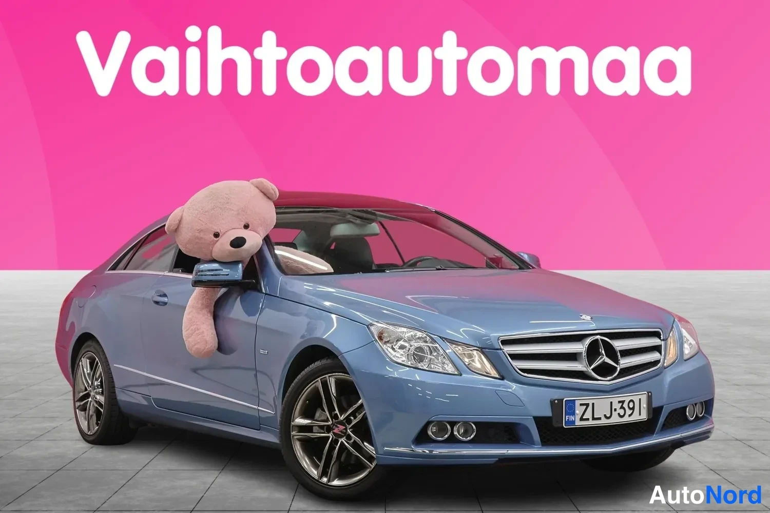 Etuviisto, nokka oikealle: Sininen Mercedes-Benzin coupé kuvattu edestä oikealta, rekisteritunnus, pehmolelu ikkunassa.