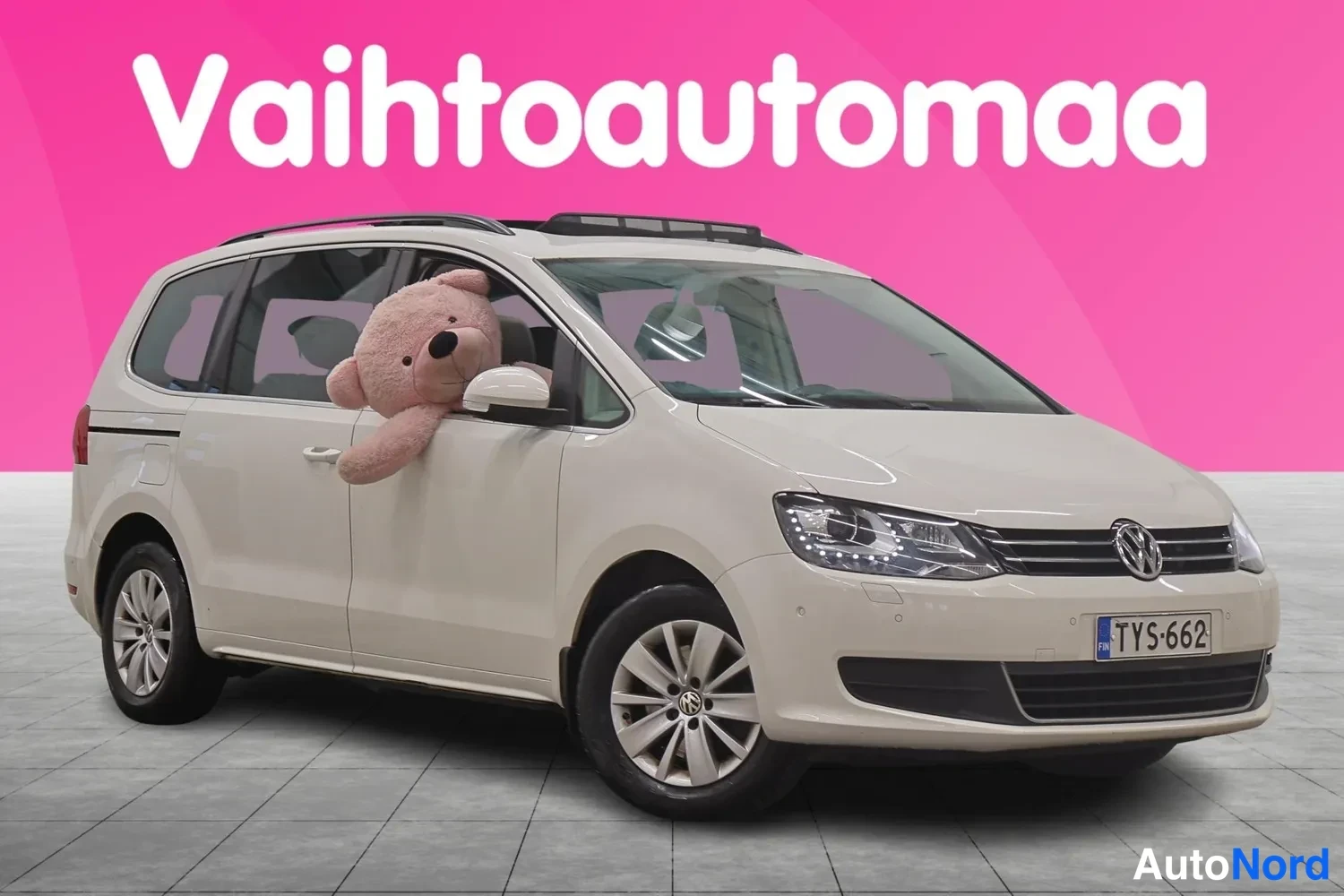 Etuviisto, nokka oikealle: Volkswagen Sharan -farmariluokan tila-auto valkoisena etukulmasta oikealta, etupanssari, kattokaiteet ja panoraamakatto näkyvissä.