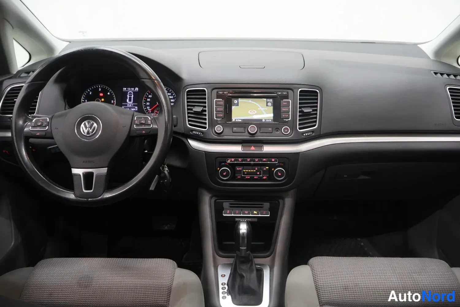 Muu: Volkswagenin ohjaamo edestä: VW-ohjauspyörä, mittaristo, navigointinäyttö keskikonsolissa ja automaattivaihteiston valitsin istuinten välissä.