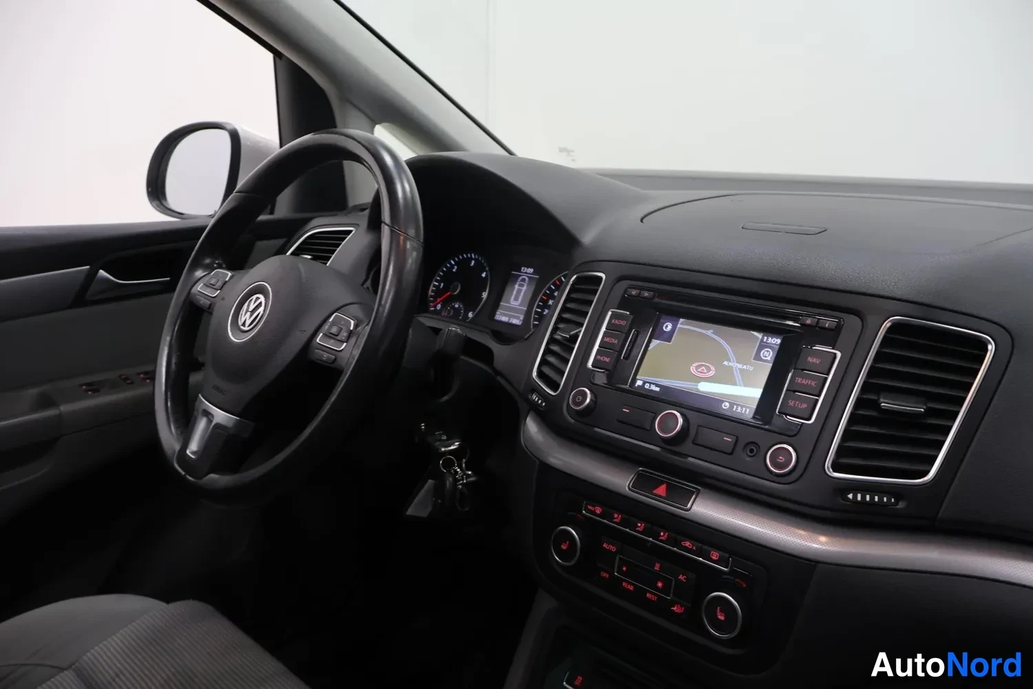 Muu: Volkswagenin ohjaamo sivulta: ohjauspyörä, mittaristo, navigointilaite näytöllä ja automaattivaihteiston valitsin, kangasistuin osittain näkyvissä.