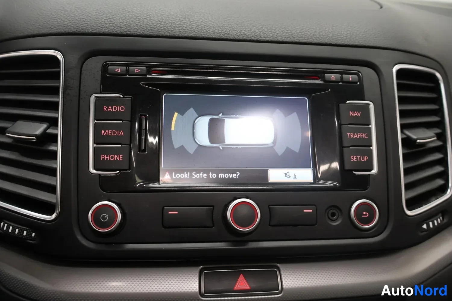 Yksityiskohta: Radionäyttö pysäköintianturinäkymässä auton kuvalla ja teksti 'Look! Safe to move?' konsolin yläosassa.