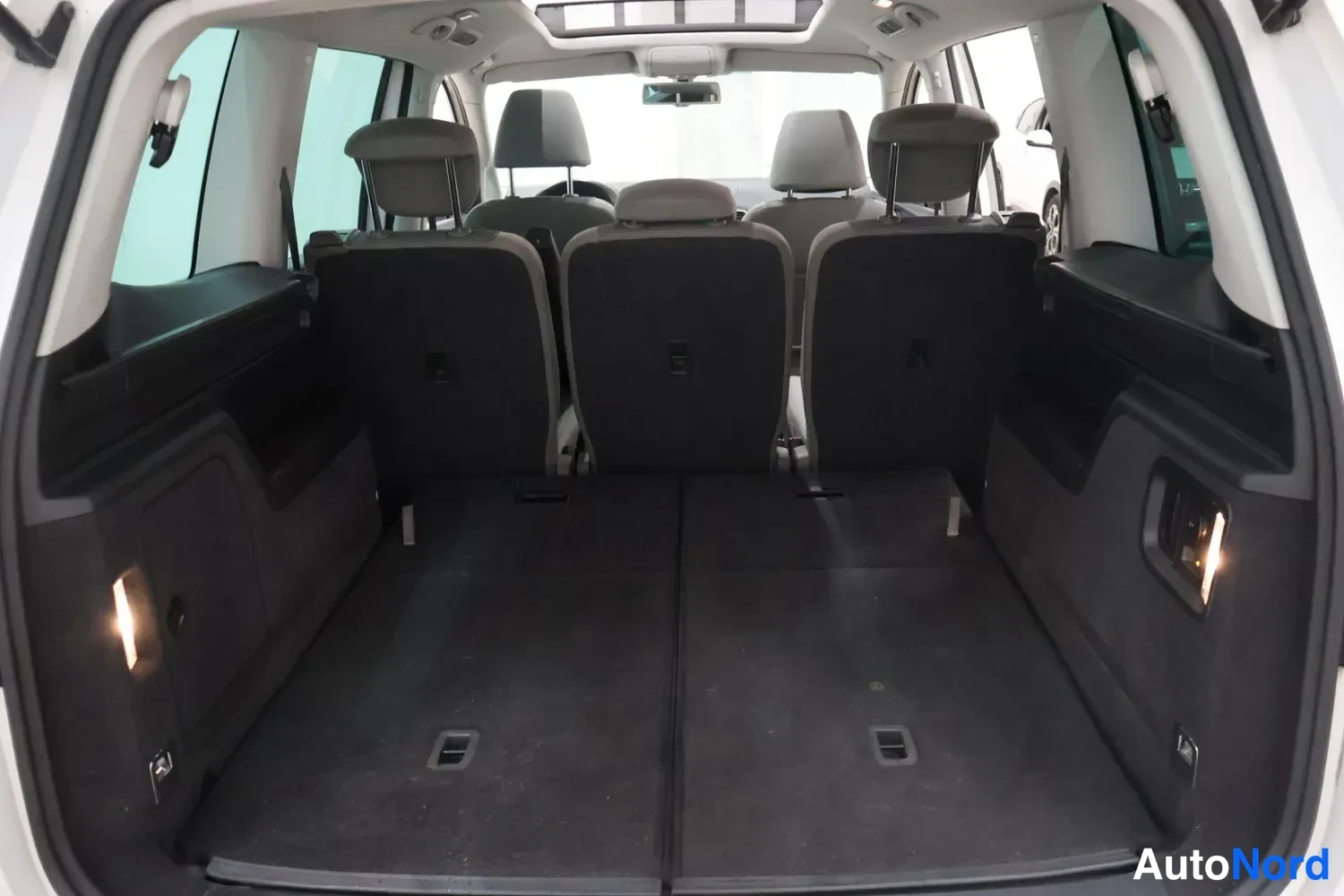 Tavaratila: Back of vehicle with third row seats up. Interior view looking forward from cargo area showing all three rows of headrests and folded middle bench.