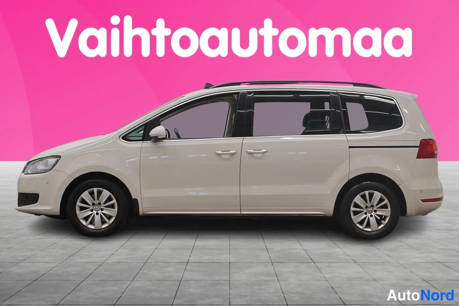 Etuviisto, nokka vasemmalle: Volkswagen Sharan -farmarimittainen tila-auto sivulta etuviistoon, vaaleanbeige kori, katse etuosasta pitkälle sivuun, katolla kromiset kiskot, studio-