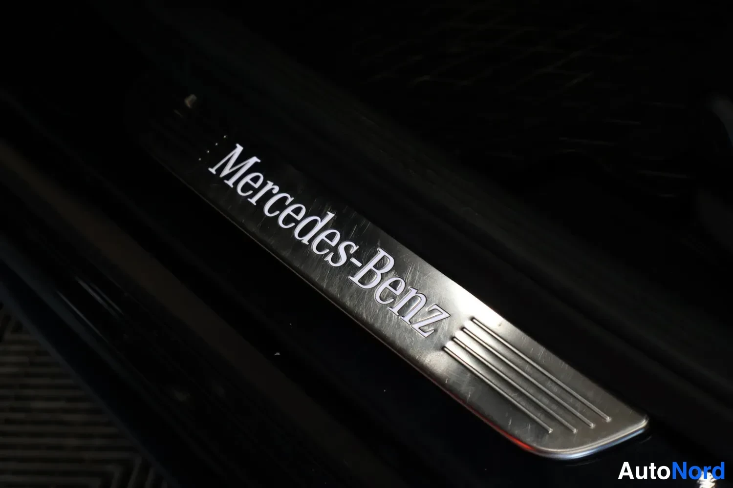 Yksityiskohta: Pohjallinen metallipohjalla, jossa valkoinen Mercedes-Benz-kirjoitus mustassa autossa.