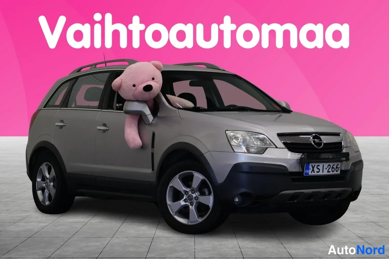 Etuviisto, nokka oikealle: Hopeanharmaa Opel Antara -maasturin etukulmakuva, punainen pehmoikä autoon