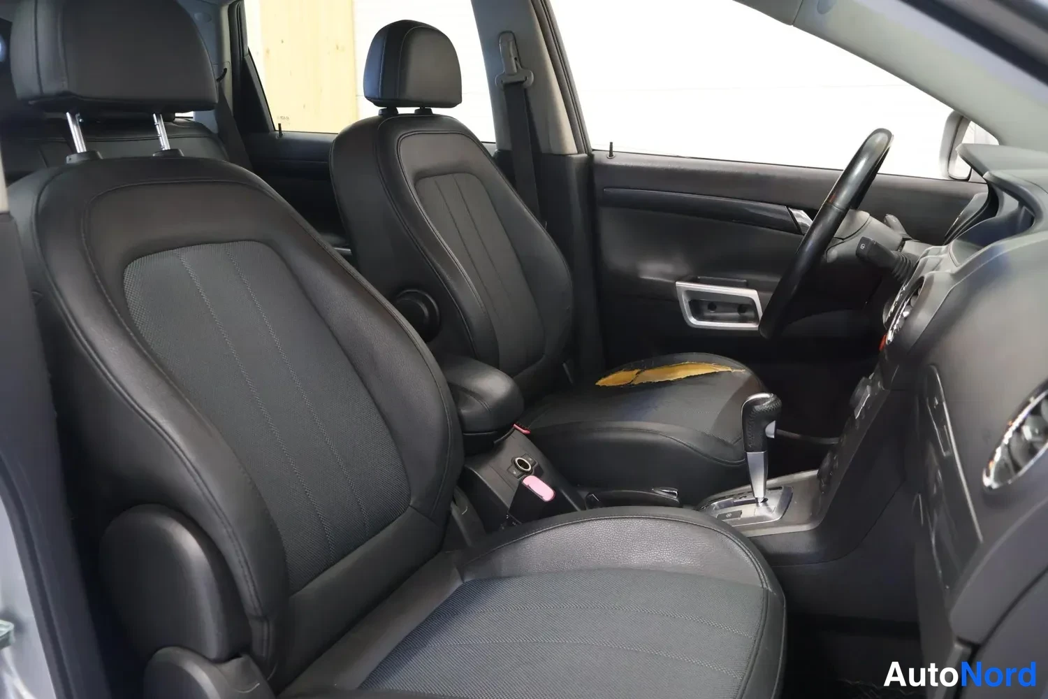 Muu: Opel Antaran etuistuimet ja keskikonsoli mustalla nahkapinnalla, automaattivaihteen valitsin ja ohjauspyörä näkyvissä.