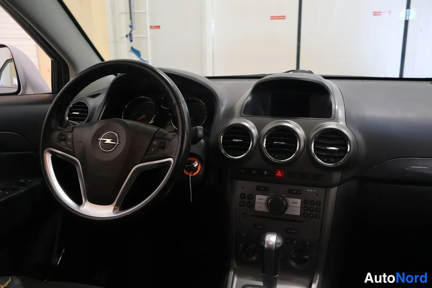 Edestä: Kuljettajan puolen näkymä auton ohjaamoon: Opel-merkkinen ohjauspyörä, kolme pyöreää suutinta ja keskikonsolin radio- ja vaihdepaneeli.