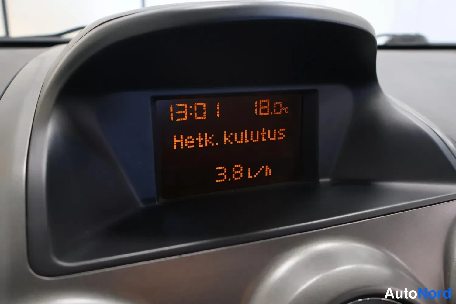 Edestä: Kojelaudan infonäyttö lähikuvassa, teksti: 13:01, 18.0 °C, Hetk. kulutus 3.8 l/h.