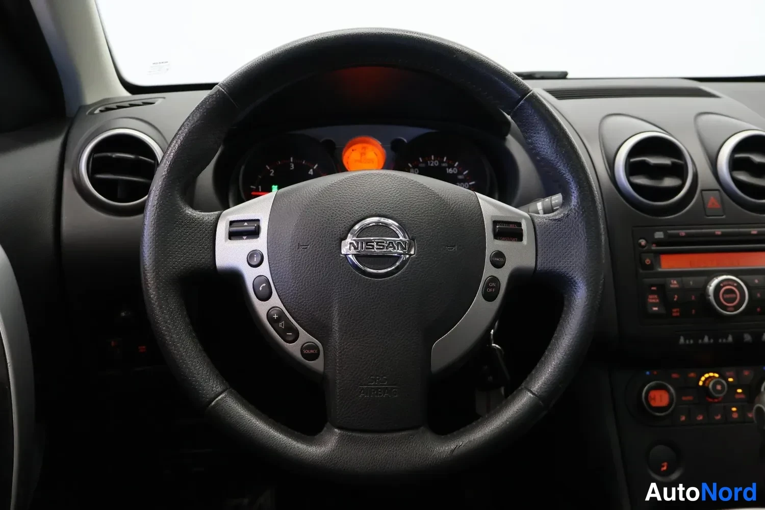 Muu: Musta Nissan-ohjauspyörä lähikuvassa mittariston ja ilmastointilievien edessä.