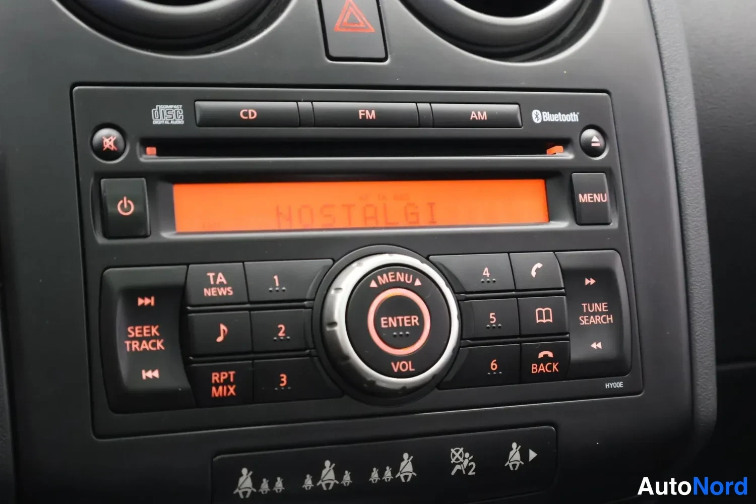 Muu: Auton radiopaneelin lähikuva: CD/FM/AM-yksikkö Bluetooth-merkinnällä, näytössä teksti NOSTALGI, sekä numeronäppäimet ja TUNE SEARCH- ja BACK-painikkeet.