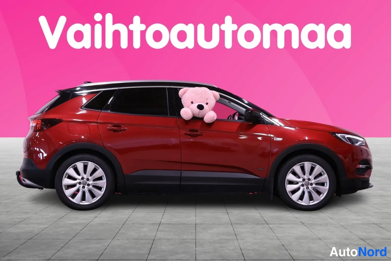 Etuviisto, nokka oikealle: Punaisen ruskean SUV-auton etukulma oikealta, pinkki tausta.
