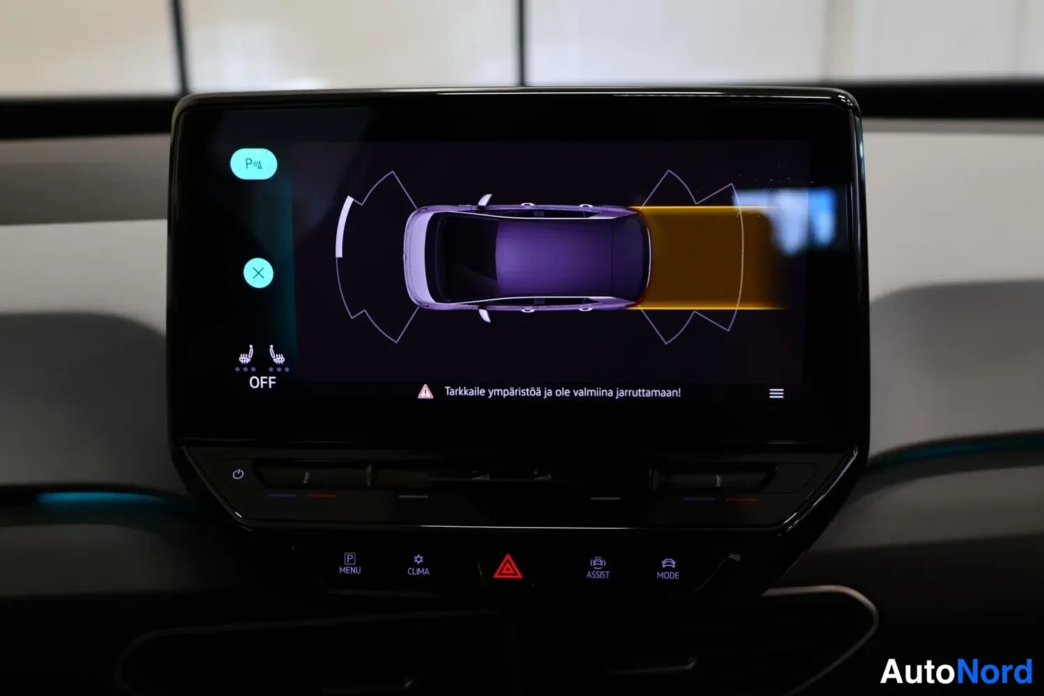 Yksityiskohta: Infotainment-näyttö pysäköintiavustajan näkymässä: auton ympäryssensorin visualisointi keltaisella ja violetilla. Ruudulla lukee 'Tarkkaile ympäristöä ja ole va