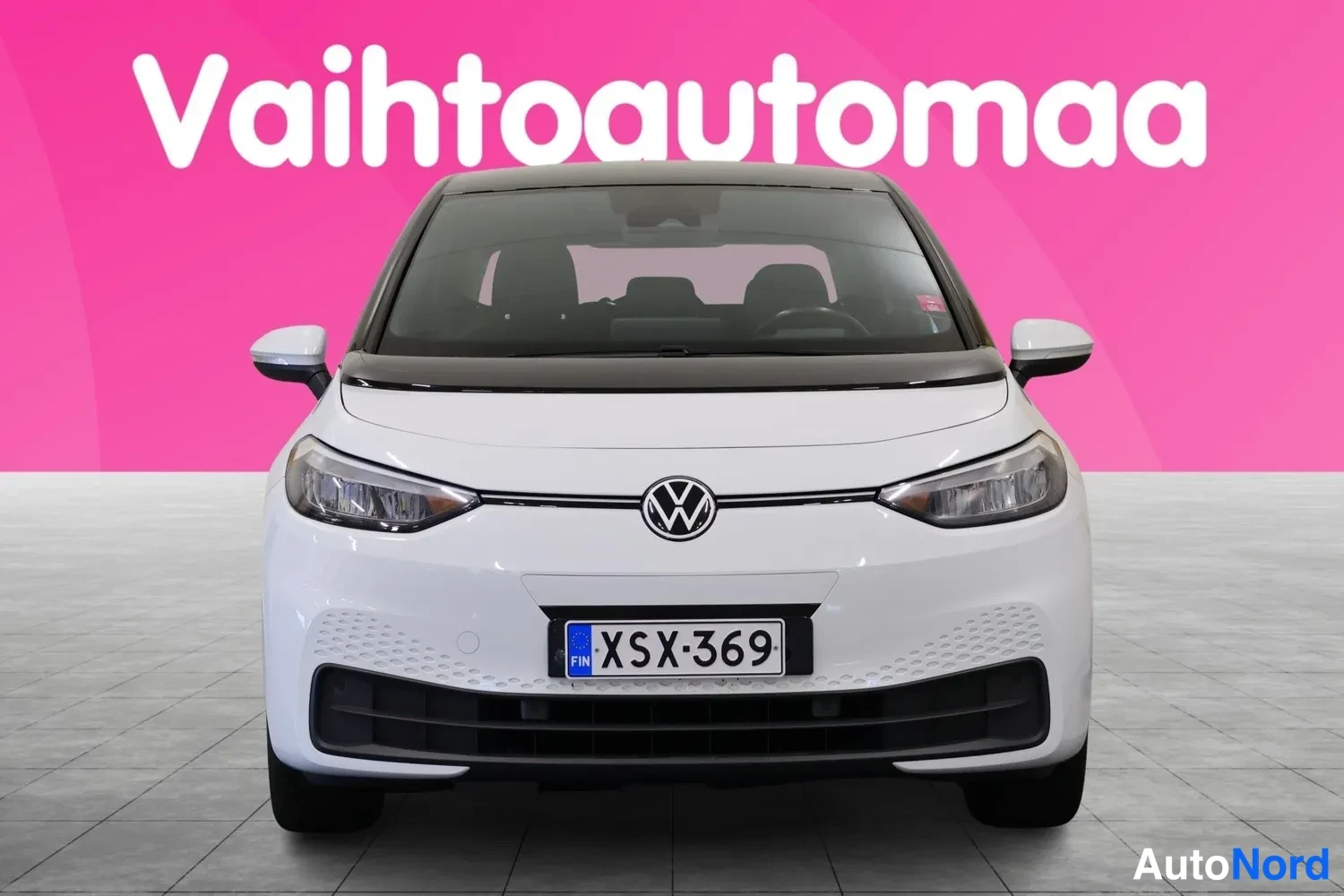 Edestä: Valkoinen Volkswagen ID.3 suoraan edestä kuvattuna, pinkki tausta.