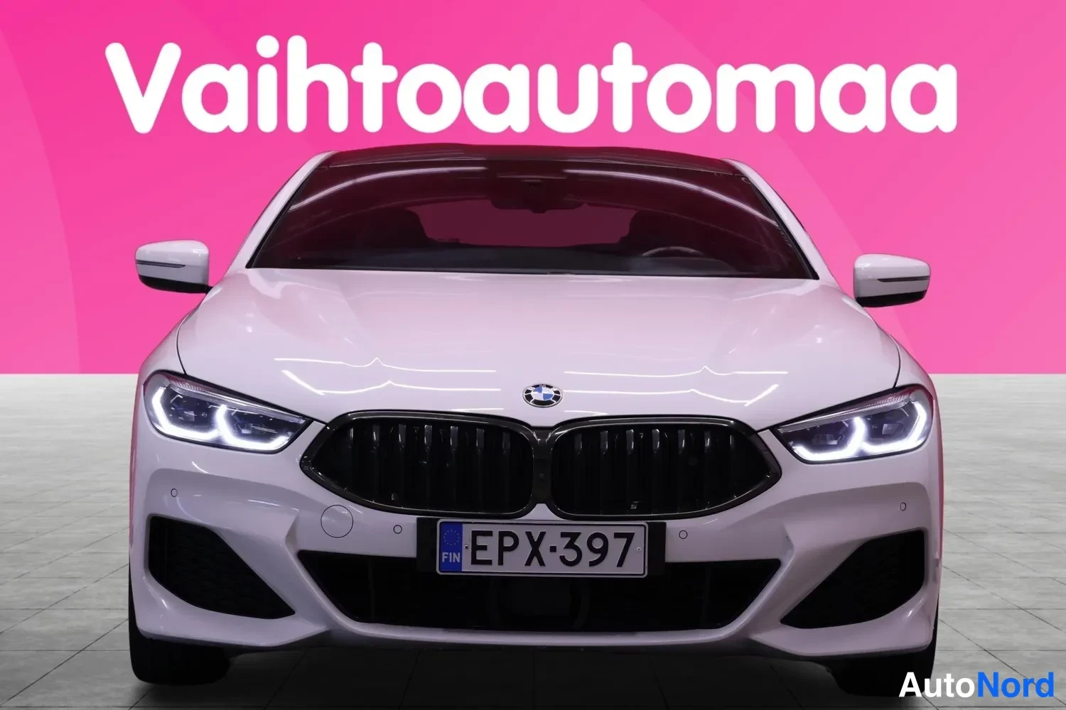 Edestä: Valkoinen BMW etukautta, tunnusvalot päällä, rekisterissä