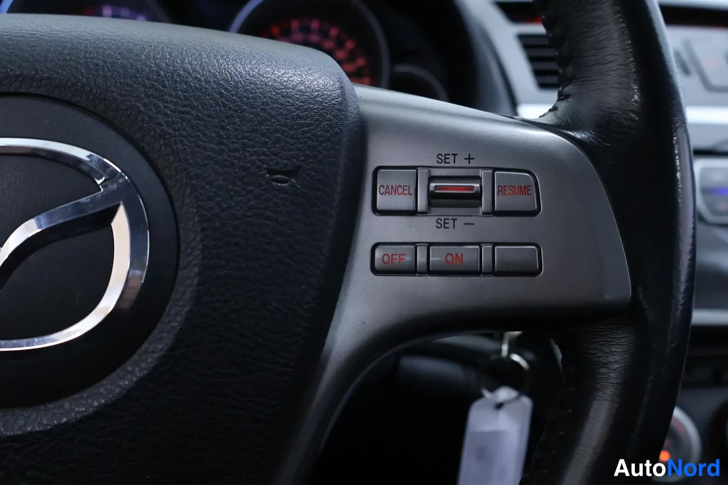 Muu: Mazda-ohjauspyörän lähikuva, jossa näkyvät vakionopeudensäätimen painikkeet SET, CANCEL, RESUME, OFF ja ON.