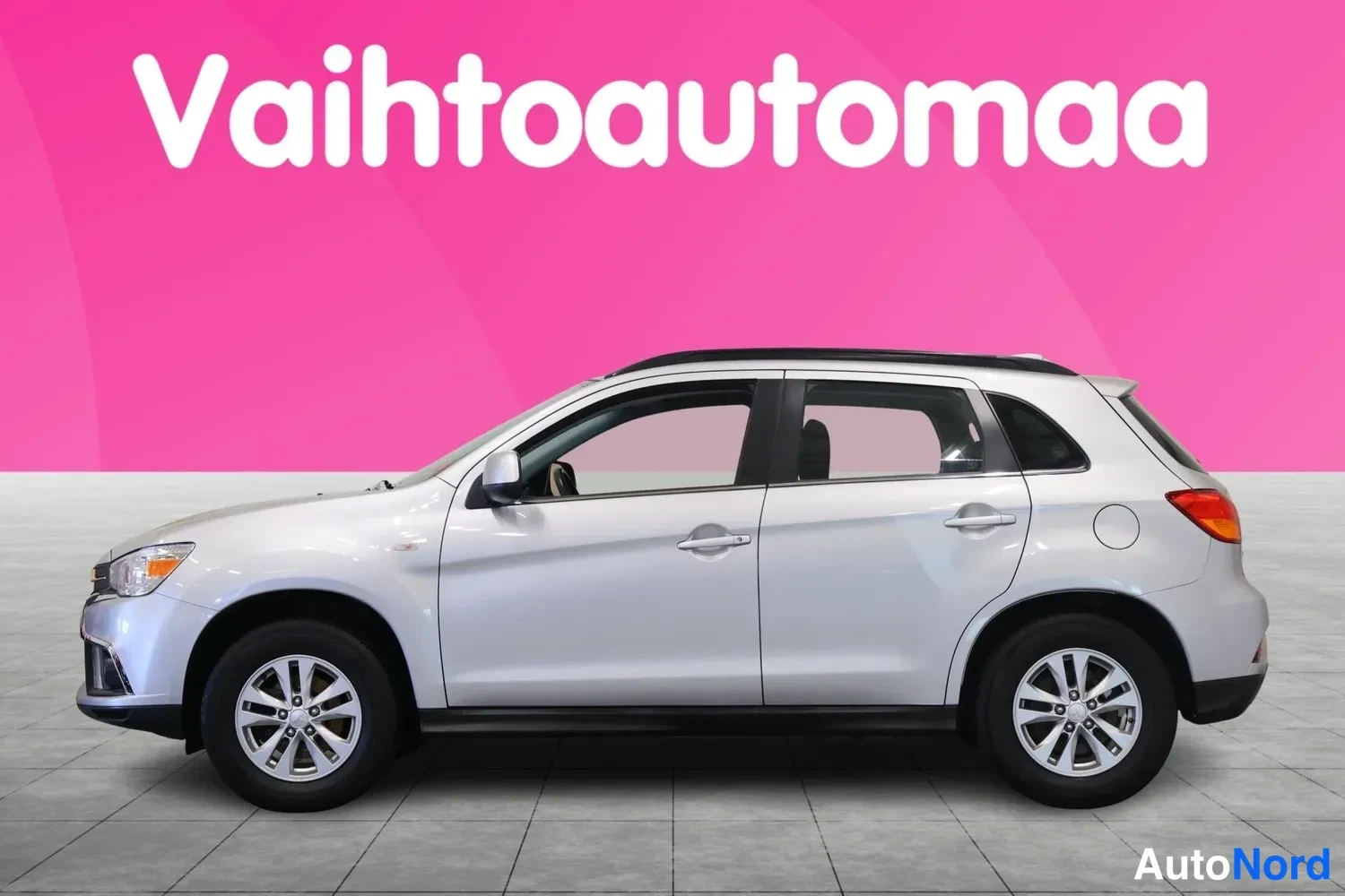Etuviisto, nokka vasemmalle: Hopeinen hatchback vasemmalta sivulta, hieman keulaa näkyvissä, pinkki tausta.