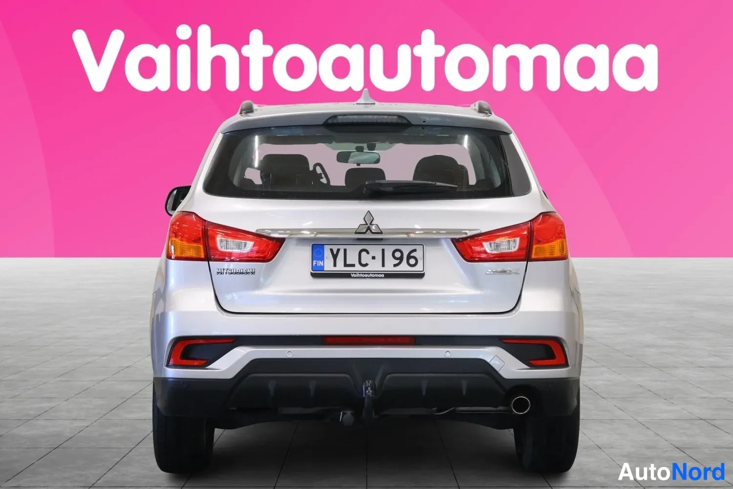 Takaa: Hopeisen hatchbackin takaosa suoraan takaa, rekisterikilpi, pinkki tausta.