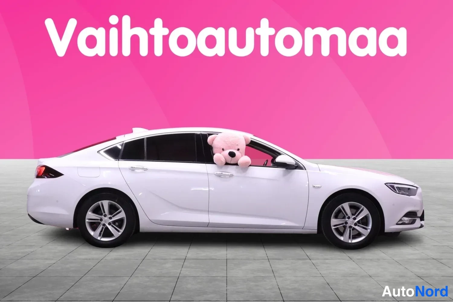 Sivulta: Valkoisen Opel Insignian sivuprofiili, keula oikealla; taustalla vaaleanpunainen Vaihtoautomaa-mainos.