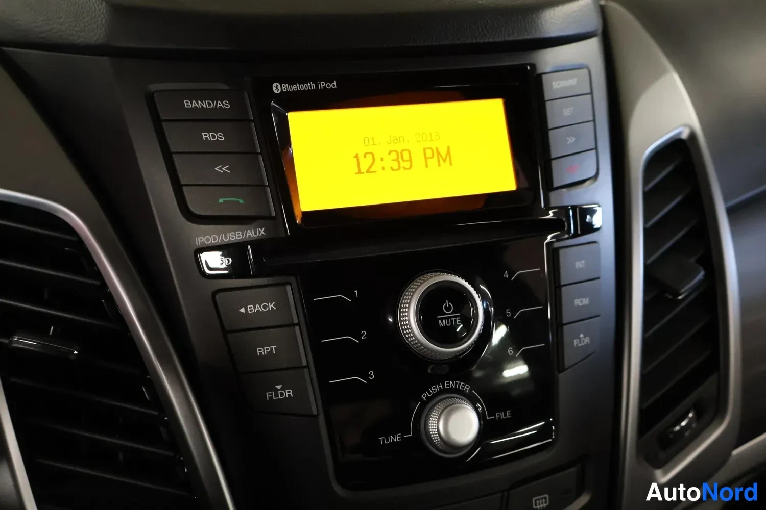 Yksityiskohta: Kojelaudan radiopaneeli näyttää ajan 12:39 PM, näytön yläreunassa tekstit Bluetooth iPod.