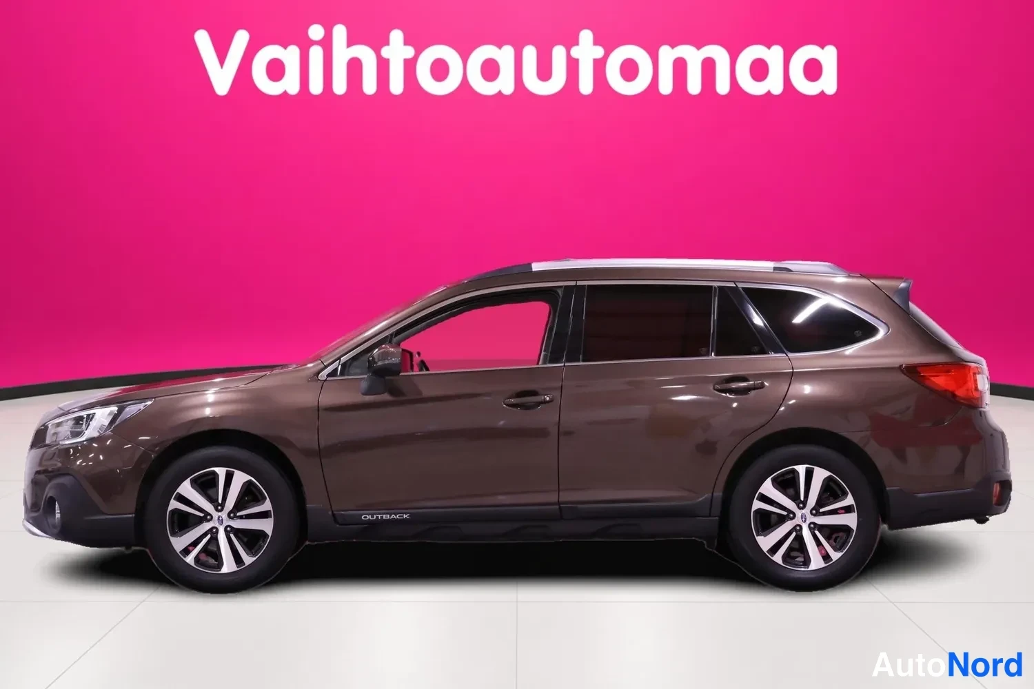 Etuviisto, nokka vasemmalle: Subaru Outback kyljeltä: tummanruskea farmarikori, kattokaiteet ja monisakaraiset alumiinivanteet.