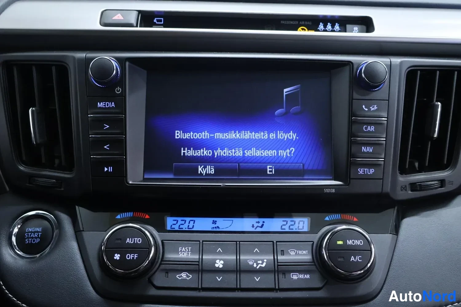 Yksityiskohta: Radio- ja ilmastointipaneeli ruudulla teksti 'Bluetooth-musiikkilähteitä ei löydy. Haluatko yhdistää sellaisen nyt?' sekä napit AUTO, OFF, MONO, A/C, NAV, SETUP