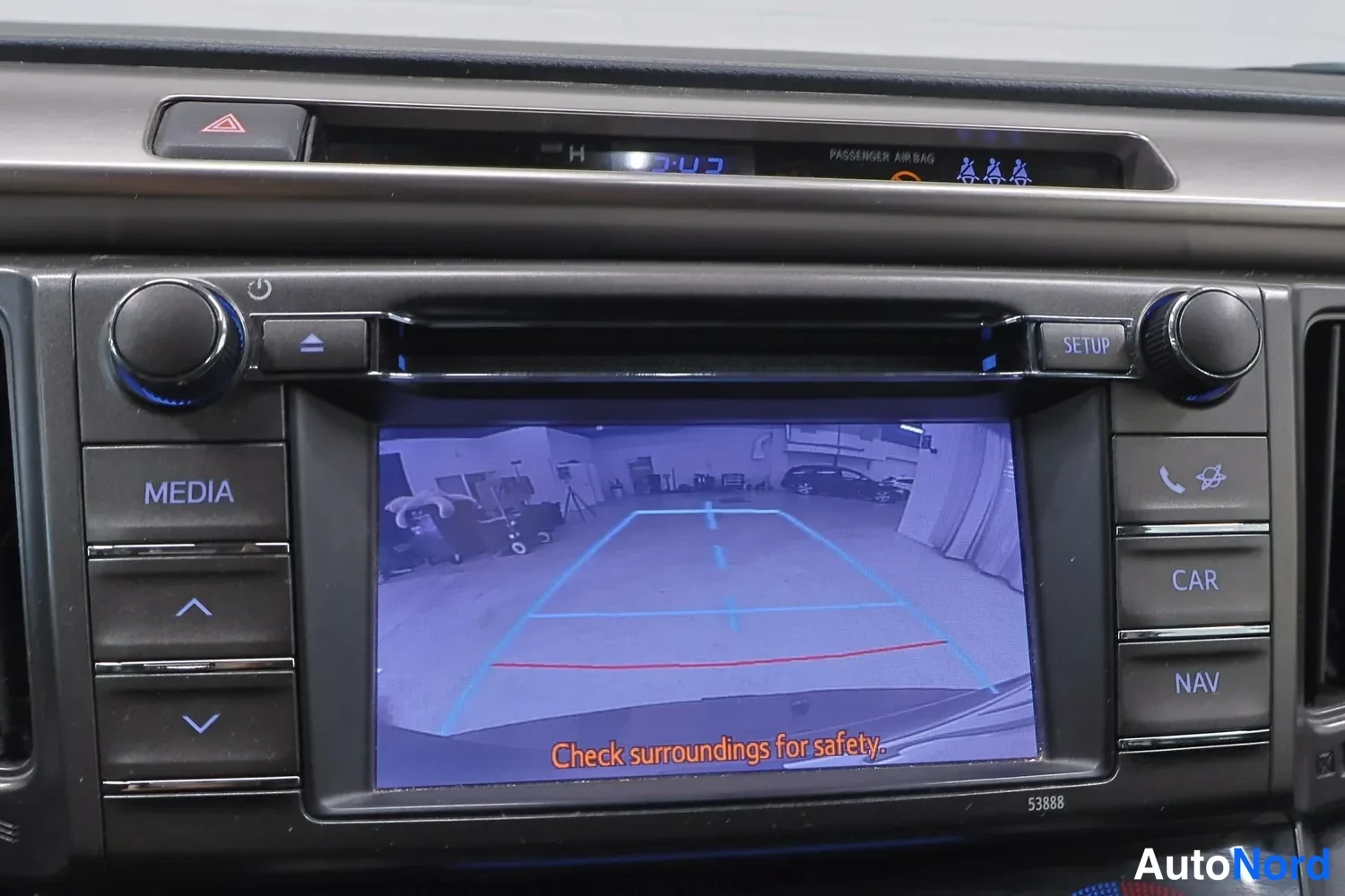 Muu: Keskiöitsimon näyttö kokoautokestävätkään kamera kuvan kanssa tekstillä 'Check surroundings for safety.', medianpainikkeet MEDIA, CAR, NAV ja SETUP.