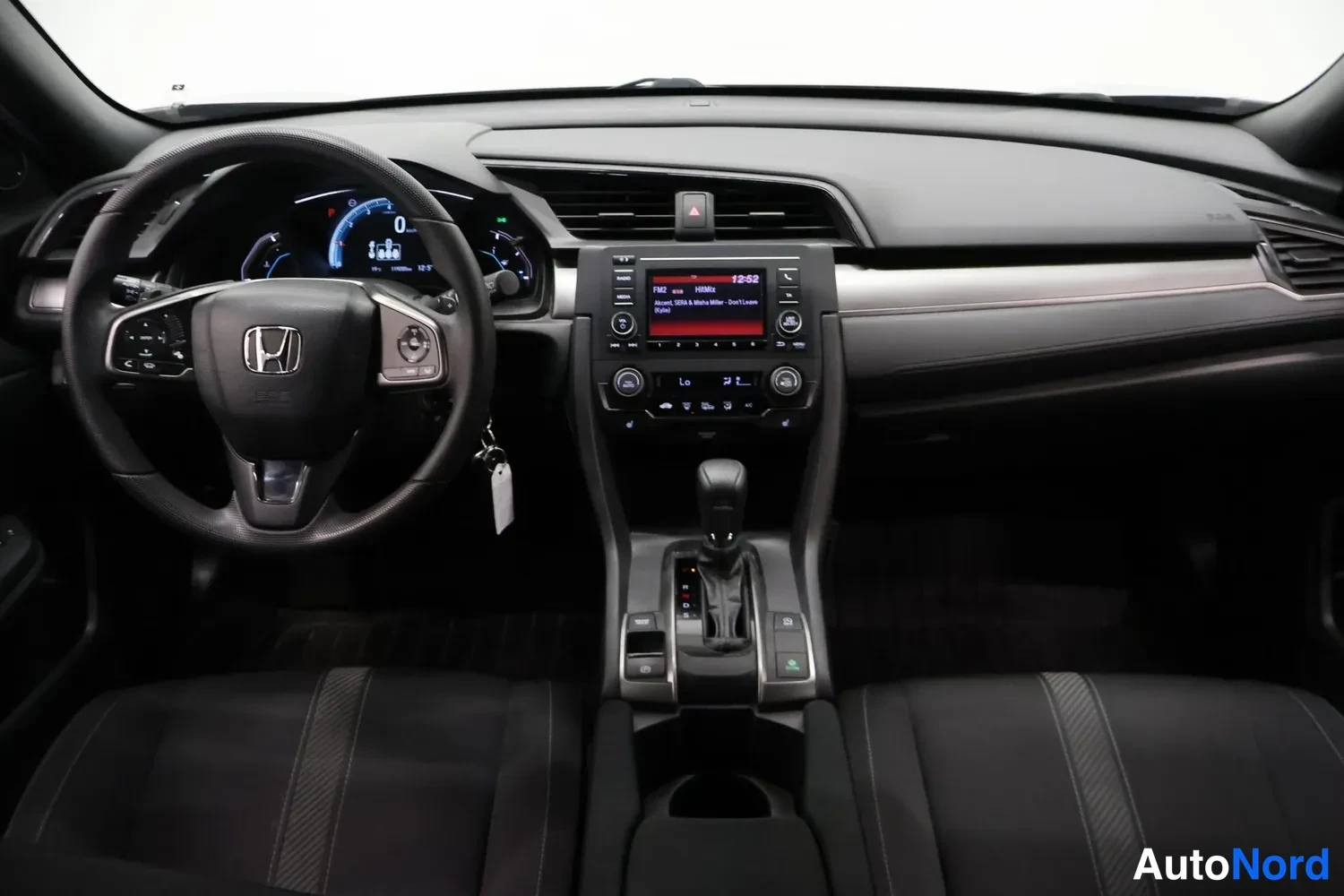 Muu: Ohjaamo näkymä: musta dashboard, Honda-ohjauspyörä, mittaristo, keskikonsoli radio-näytöllä ja automaattivaihteiston valitsin.