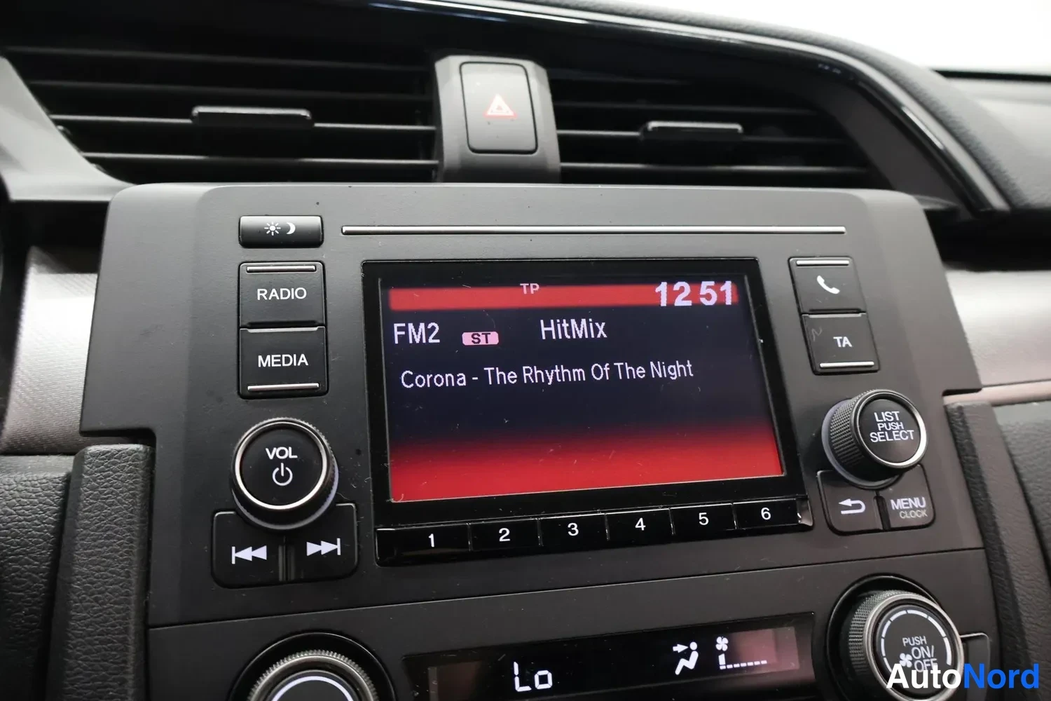 Yksityiskohta: Auton keskuskojeiston lähikuva: radion näytöllä kanava FM2 HitMix, soittaa Corona – The Rhythm Of The Night, kello 12:51. Näkyvissä RADIO-, MEDIA- ja VOL-painik