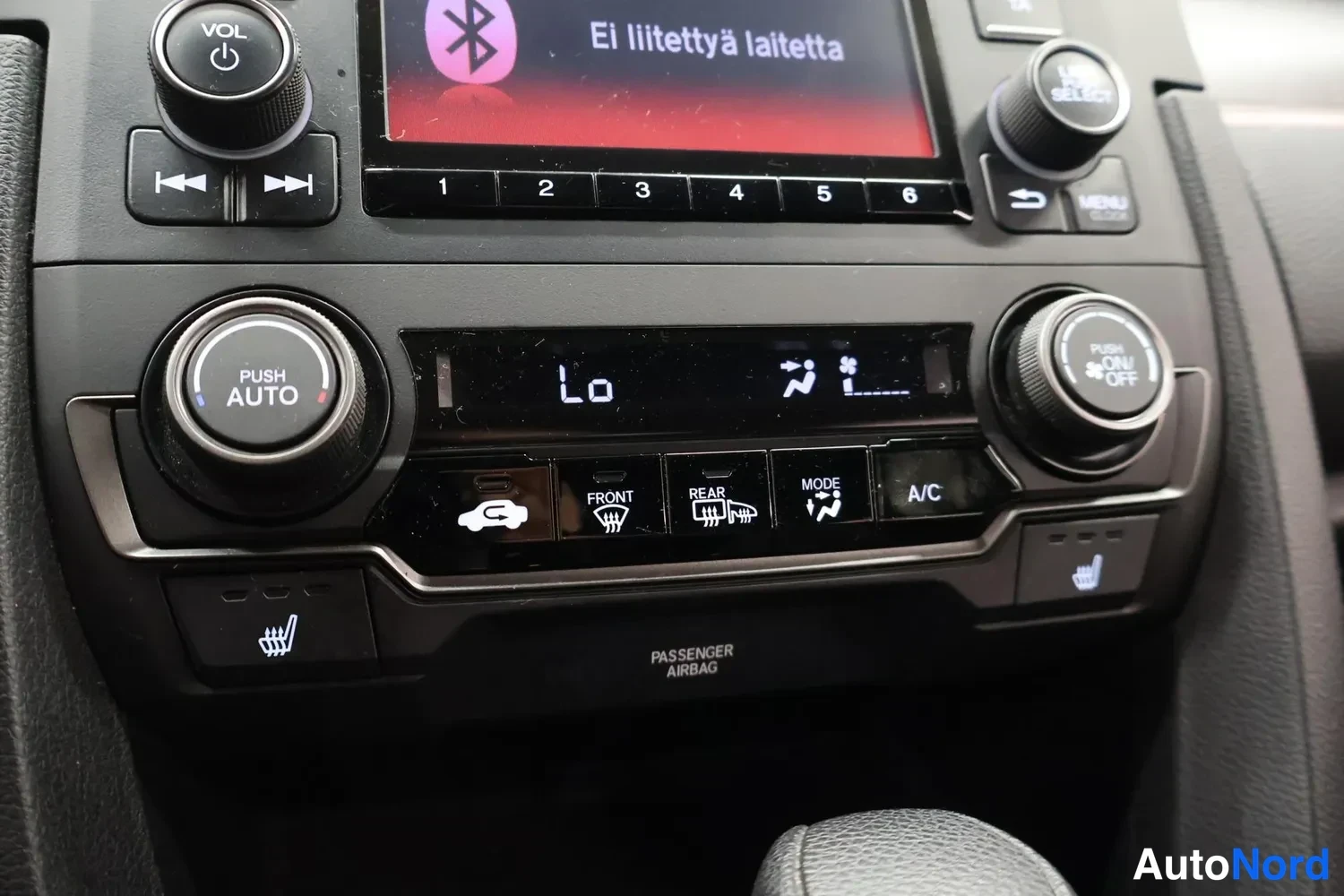 Yksityiskohta: Kojelaudan ilmastointipaneeli lähikuvassa: näytössä lukee 'Ei liitettyä laitetta', säädinmerkinnät PUSH AUTO, FRONT, REAR, MODE ja A/C, sekä lämmitettävien istu