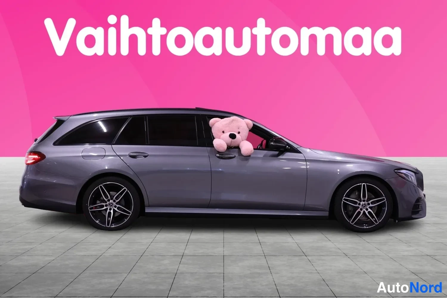 Sivulta: Autosta on kuvattu profiili. Siinä on hopeanharmaa väri, neliovinen karossi, tummennetut ikkunat ja kevytmetallivanteet. Taustana on vaaleanpunainen seinä.