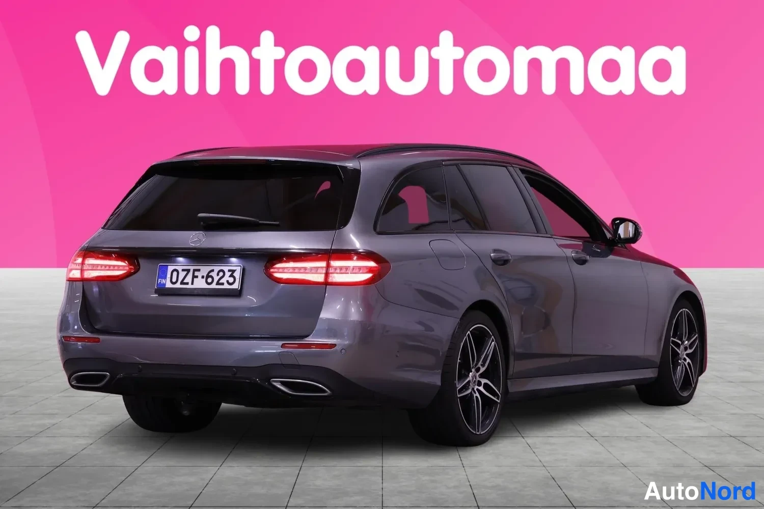 Takaviisto: Takaa ja oikeasta kulmasta otettu kuva samasta hopeanharmaasta Mercedes-Benz-tilavasta autosta. Takavalot on sytytetty, rekisterinumero on selkeästi näkyvissä t