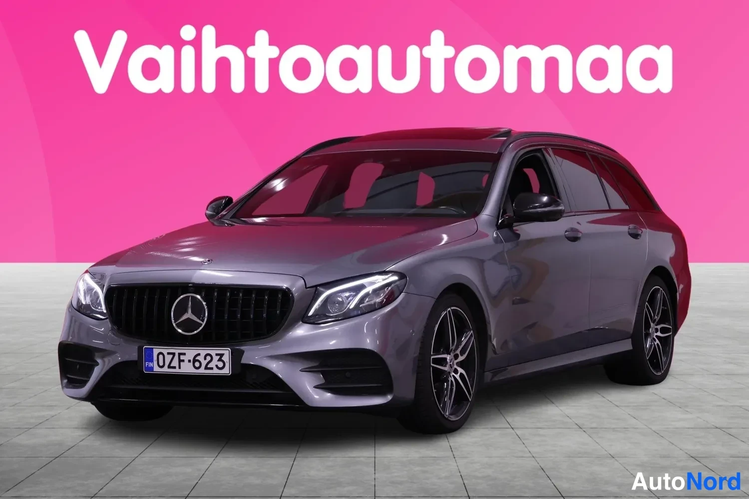 Etuviisto, nokka vasemmalle: Mercedes-Benz E 300d -farmari etuviistosta, harmaa kori, musta etusäleikkö ja rekisterikilpi.