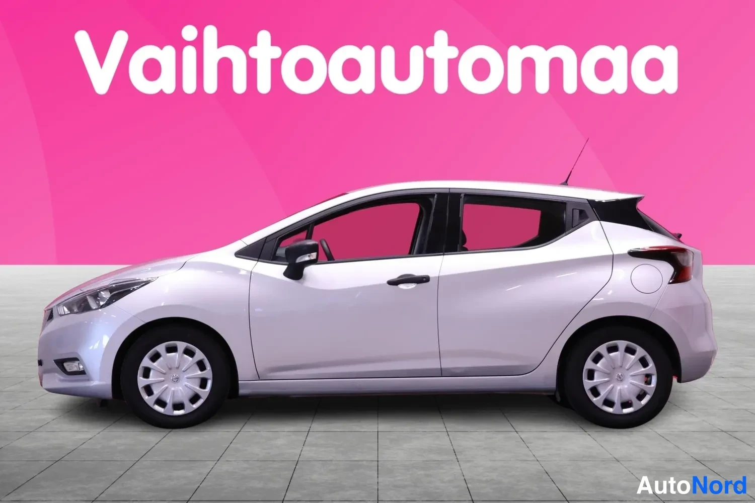Etuviisto, nokka vasemmalle: Hopeanvärinen Nissan Micra -henkilöauto sivulta etukulmasta, nokka vasemmalla, vaaleaa taustaa vasten.