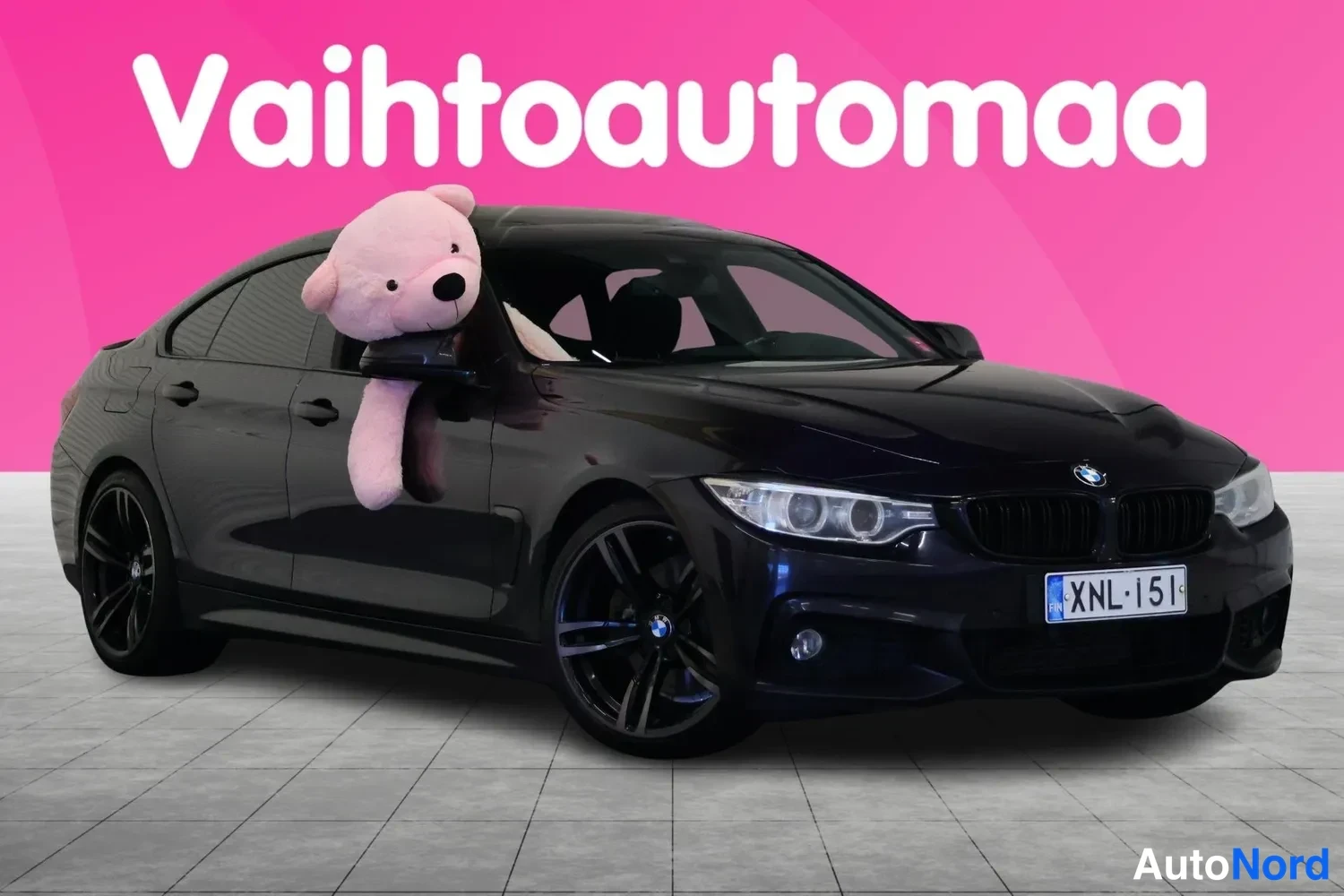 Etuviisto, nokka oikealle: Musta BMW Gran Coupé -mallinen auto valmiissa etukulmakuvassa, pinkki tausta ja pehmolelu ikkunassa.